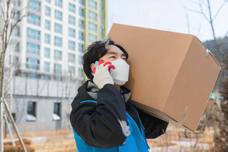 Asian delivery man with mask on phone with customer