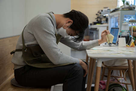depressed Asian male entrepreneur, store owner with mask with bills, business  conceptの写真素材