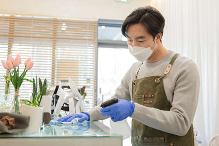 Asian man with mask sanitizing storeの写真素材