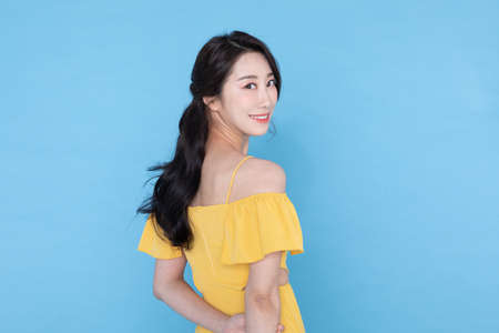 side view of smiling beautiful Korean Asian woman in summer yellow dress, skyblue backgroundの写真素材