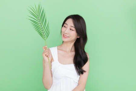 beauty concept, beautiful Korean Asian woman with green leaves, mint color backgroundの写真素材
