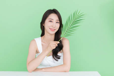 beauty concept, beautiful Korean Asian woman with green leaves, mint color backgroundの写真素材