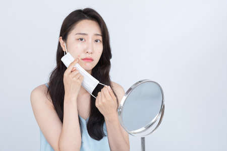 Asian woman with acne, pimple skin trouble on cheek due to wearing mask in covid eraの写真素材