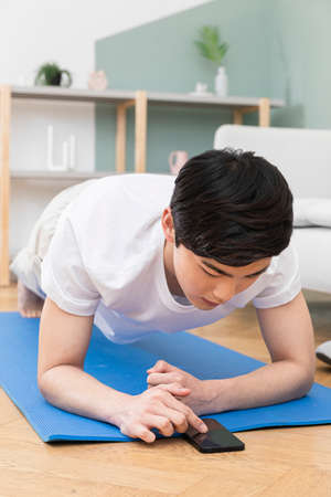 Asian man doing plank through online fitness coaching classの写真素材