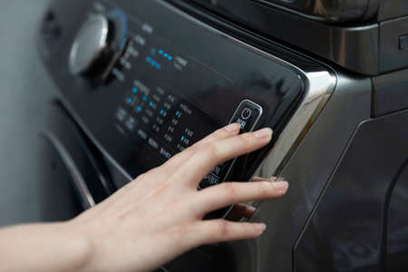 Hand pressing the washing machine power switchの写真素材
