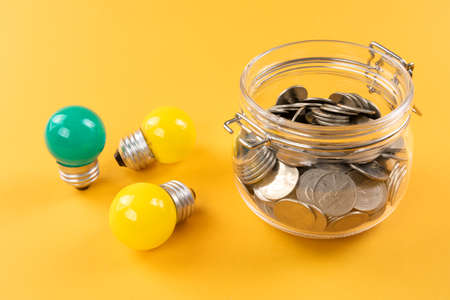 Yellow, green mini bulbs and coins on yellow background, eco energy concept