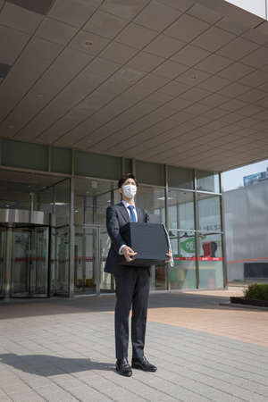 Asian man employee with mask leaving office with box due to lay off, covid 19 effects in business