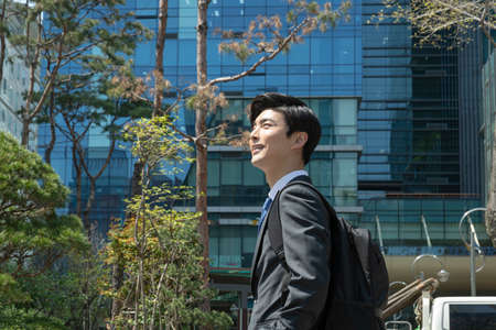 lively, cheerful Asian handsome man looking at company building, business concept