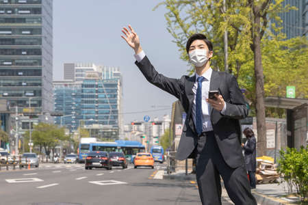 Asian young man with mask catching taxiの写真素材