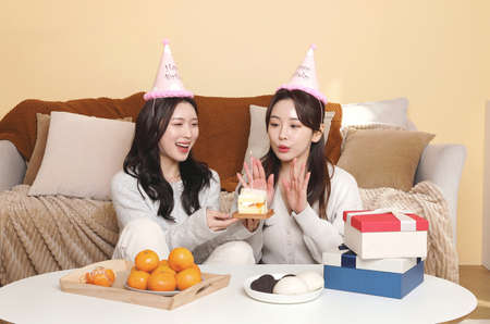 asian korean women best friends celebrating birthday, blowing cake candlesの写真素材