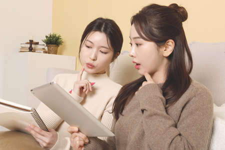 asian korean women friends attending online class, watching video tutorial with tablet, streamingの写真素材