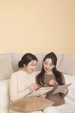 asian korean women friends attending online class, watching video tutorial with tablet, streamingの写真素材
