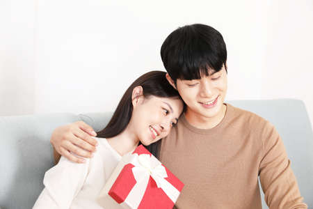 Asian Korean couple on sofa exchanging gifts, holiday season and shopping concept