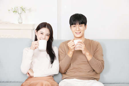 sweet Asian Korean couple on sofa drinking tea