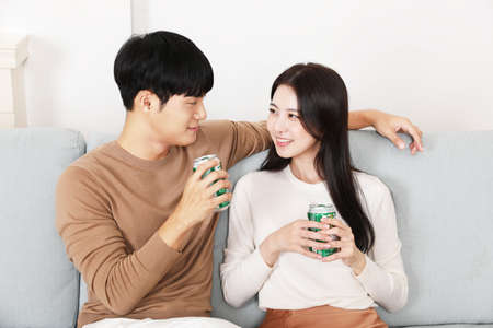 Asian Korean couple drinking bear on sofa, winter cozy home date concept