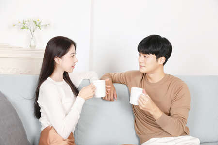sweet Asian Korean couple on sofa drinking teaの写真素材