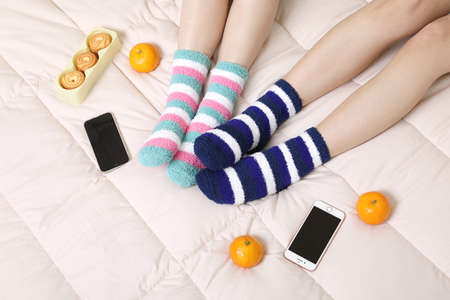 eating fruits on the bed, eating snacks, smartphones, and sleeping socks. winter season concept, two beautiful Asian Korean womenの写真素材