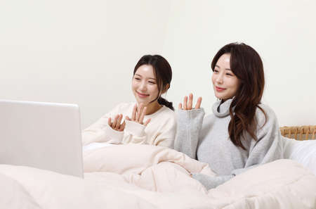winter season concept, two beautiful Asian Korean women making video calls on their laptop on bed