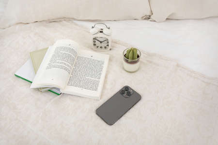 relax cozy objects and background with smart phone, a book. candle, clock, beddingの写真素材