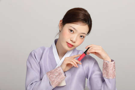 spring beauty concept, beautiful korean woman wearing hanbok with holding a lip tintの写真素材
