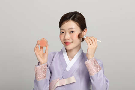 spring beauty concept, beautiful korean woman wearing hanbok putting on the blusherの写真素材