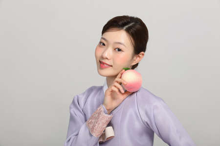 spring beauty concept, beautiful korean woman wearing hanbok with holding a peachの写真素材