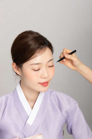 spring beauty concept, beautiful korean woman wearing hanbok getting makeupの写真素材