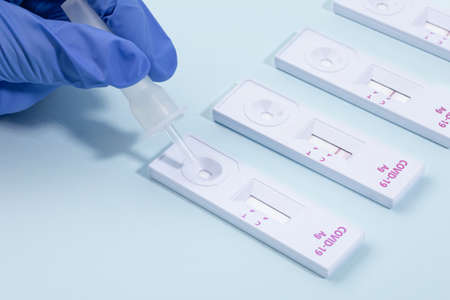 hand dropping specimen solution into the covid test kit, blue background
