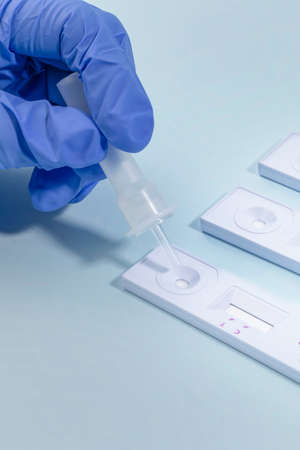 hand dropping specimen solution into the covid test kit, blue background