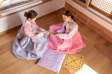 Korean and Caucasian girls wearing Hanbok playing Yut, Korean traditional board game