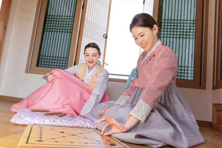Korean and Caucasian girls wearing Hanbok playing Yut, Korean traditional board game