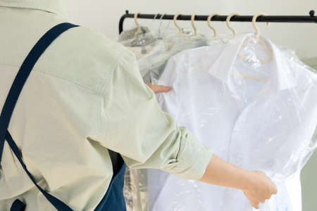 aesthetic laundry concept_person checking the rack with clean shirts in plastic bags after dry cleaningの写真素材