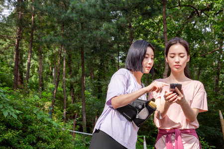 two Korean Asian female friends in 20s hiking and plogging in mountain__path finding using smartphoneの写真素材
