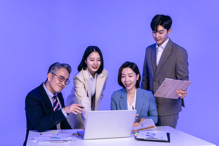 Asian Korean senior, middle aged and young male and female colleagues models in business attire, neon purple studio background, meeting while looking at a laptopの写真素材