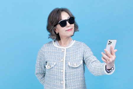 active young senior Korean Asian woman with sunglasses using smartphone