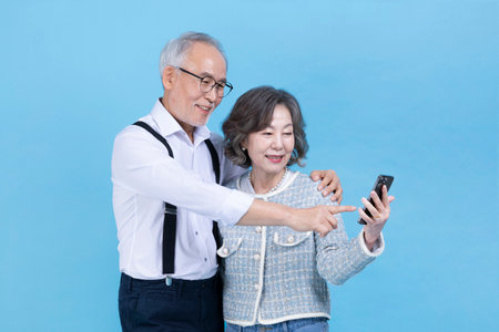 active young senior Korean Asian couple looking at smartphoneの写真素材