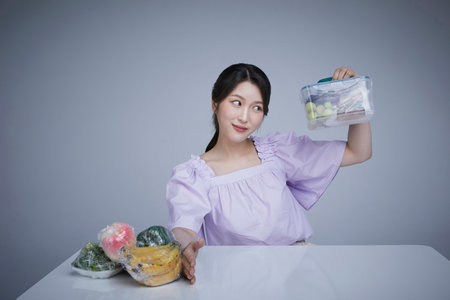 Image of a korean asain beautiful woman holding a plastic tub of fruits and vegetables wrapped in  wrap.の写真素材