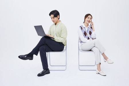 A man and a woman sitting in a chair playing a laptop and a smartphone