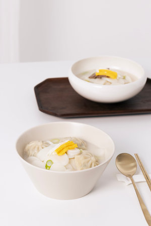 Two bowls of rice cake soup and a spoon are placed on a white table