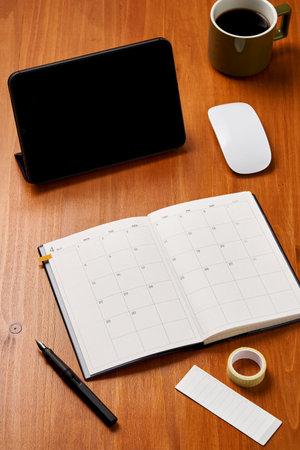 a diary and tablet PC on a wooden deskの写真素材