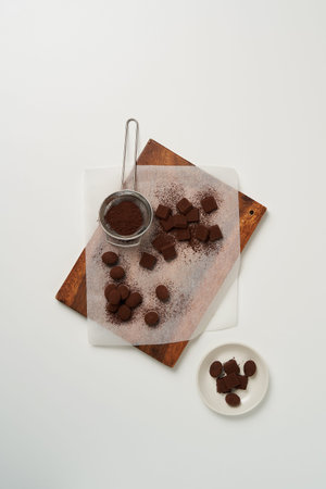 There are pieces of homemade chocolate sprinkled with cocoa powder on the cutting board and a...