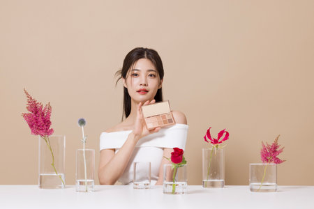 a woman in her 20s holding cosmetics in front of a table decorated with flowersの写真素材