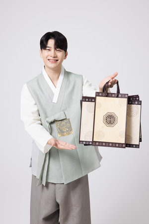Portrait of a young man wearing hanbok and holding shopping bagsの写真素材