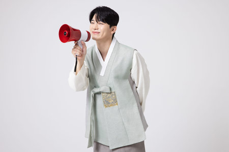 A young man wearing a hanbok and shouting while holding a megaphoneの写真素材