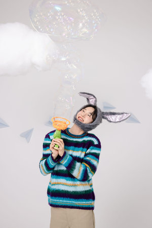 Portrait of a man standing wearing a rabbit hat and holding soap bubblesの写真素材