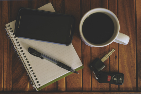 Cup Of Coffee, Cell Phone, Notepad, Pen, And Keys On A Wood Tableの写真素材