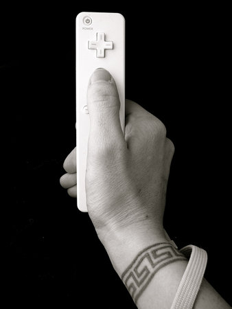 Hand with wrist tattoo holding video game control over black background