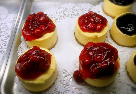 Miniature Strawberry and Blueberry Cheesecakes Displayed on Bakery Trayの写真素材