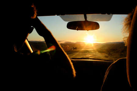 A man and woman drive their car into the sunsetの写真素材