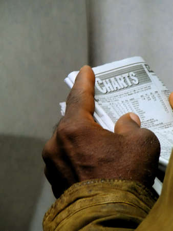 Detail of man with dirty sleeve reading horse racing charts in the daily newspaperの写真素材